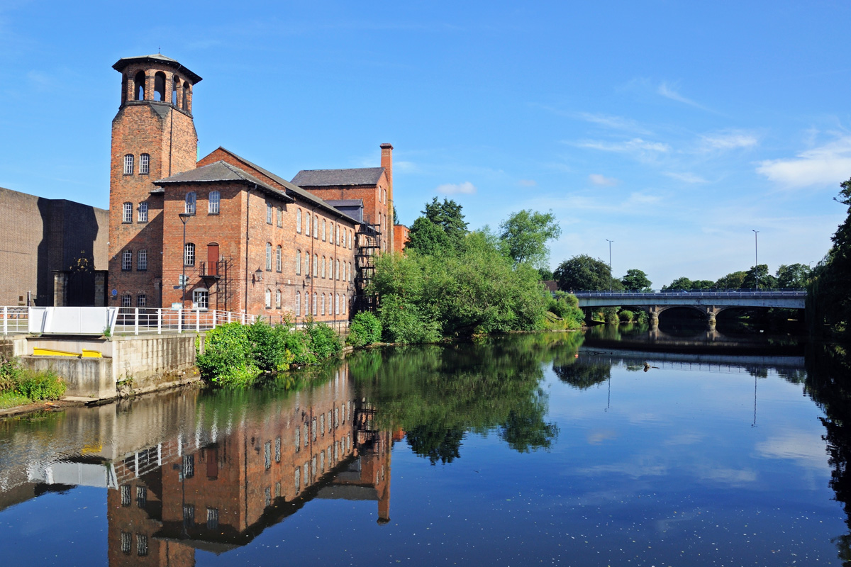 The Silk Mill sits alongside the River Derwent in the city of Derby in Derbyshire on a bright, summer day.