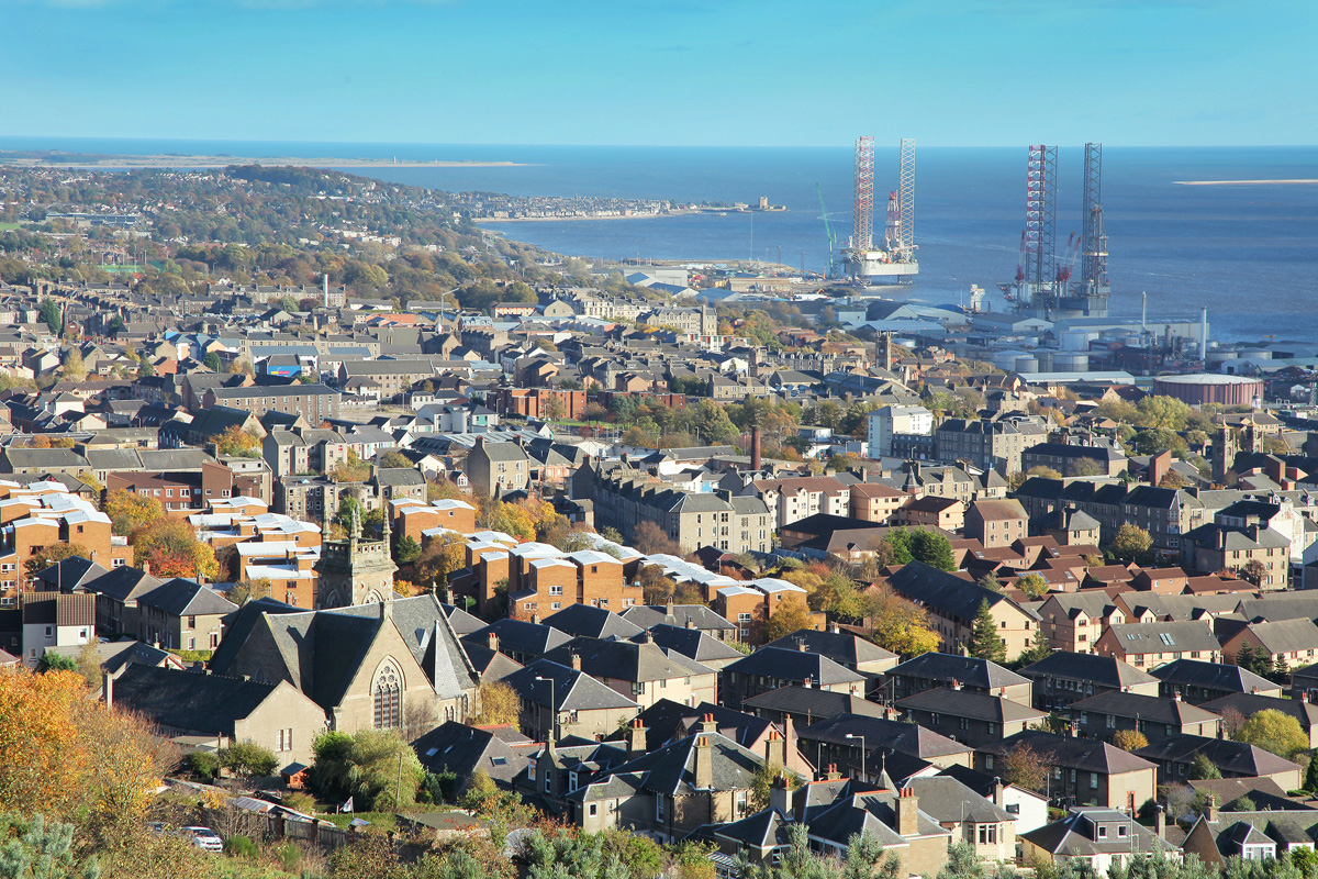 A raised view of the roof tops of the city of Dundee, leading out to the ocean.