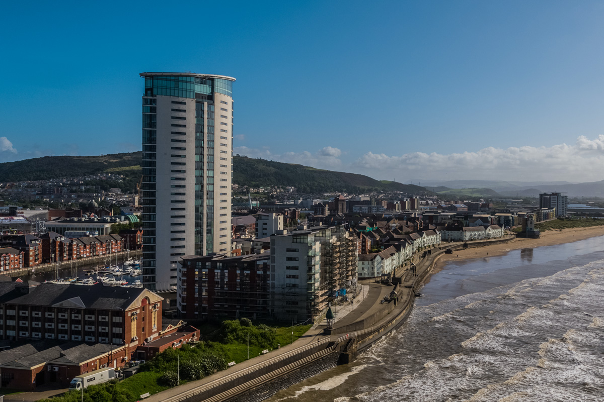 Aerial view of the sea breaking on the coastline of Swansea Bay with Swansea city centre further in.